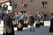 Een vaandeldrager draagt het adelaarsvaandel naast een geestelijke in bordeauxrood