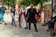 Diverse coppie medievali ballano in girotondo in una piazza alberata di Bailo