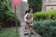 Una bambina in tunica bruna corre lungo il sentiero accanto al muro