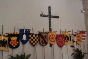 Una raccolta di scudi e gonfaloni pende dal muro sotto la croce