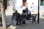 Persone anziane conversano su una panchina mentre passano abitanti in costume