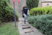 Un bambino salta sopra i tronchi su un sentiero accanto al muro medievale