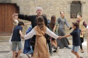Un uomo in costume guida un girotondo di bambini davanti a una facciata