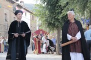 Un notaio e un chierico conversano in una via in costume d'epoca