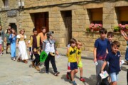 Alcuni bambini sfilano per una via con vasi di gerani in fiore