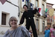 Un trampoliere fa equilibri per strada accanto a un'abitante sorridente