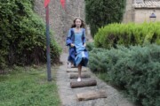 Una bambina in costume azzurro salta fra tronchi di legno