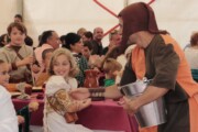 Un uomo distribuisce acqua ai bambini durante il pranzo popolare medievale