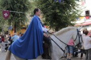 Un cavaliere con mantello azzurro percorre le vie con il corteo reale