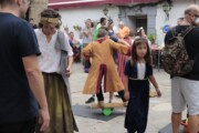Abitanti in costume si mescolano accanto a un gioco d'equilibrio nella piazzetta