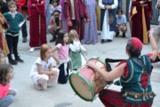 Bambini circondano un giullare che suona un grande tamburello rosso